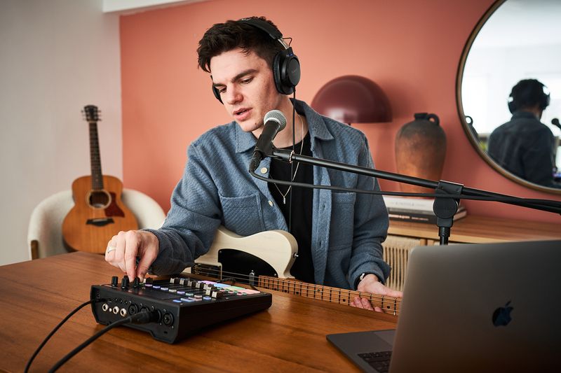 Un homme avec des écouteurs joue du clavier devant une guitare acoustique.